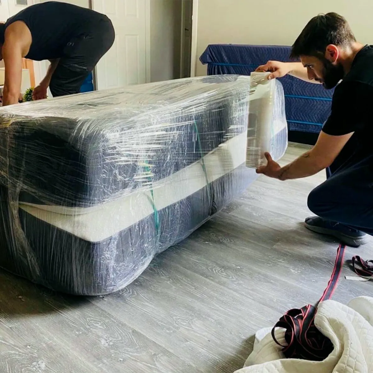 Two movers shrink-wrapping a mattress before carrying it out