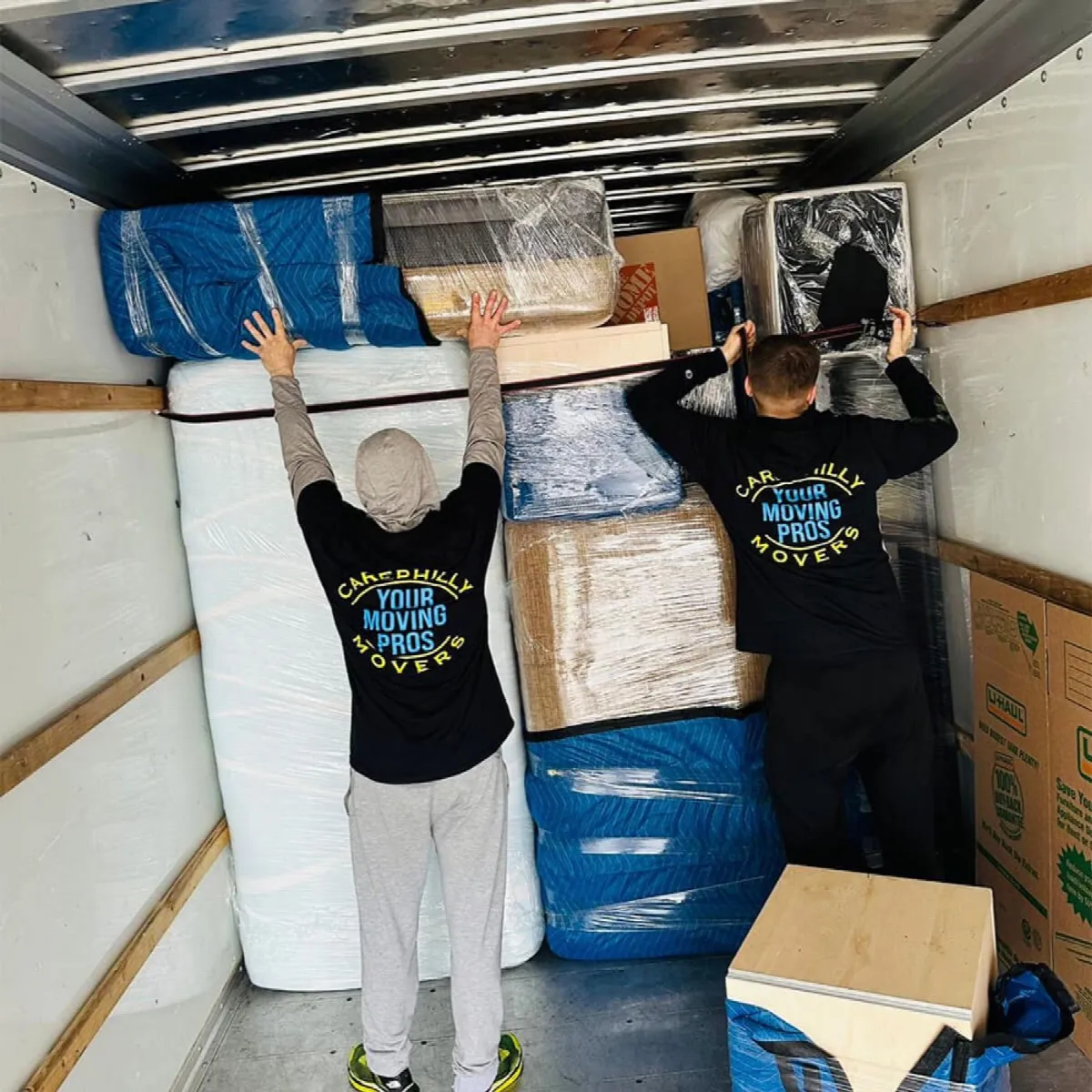 Two movers tightening a cargo strap across a loaded truck