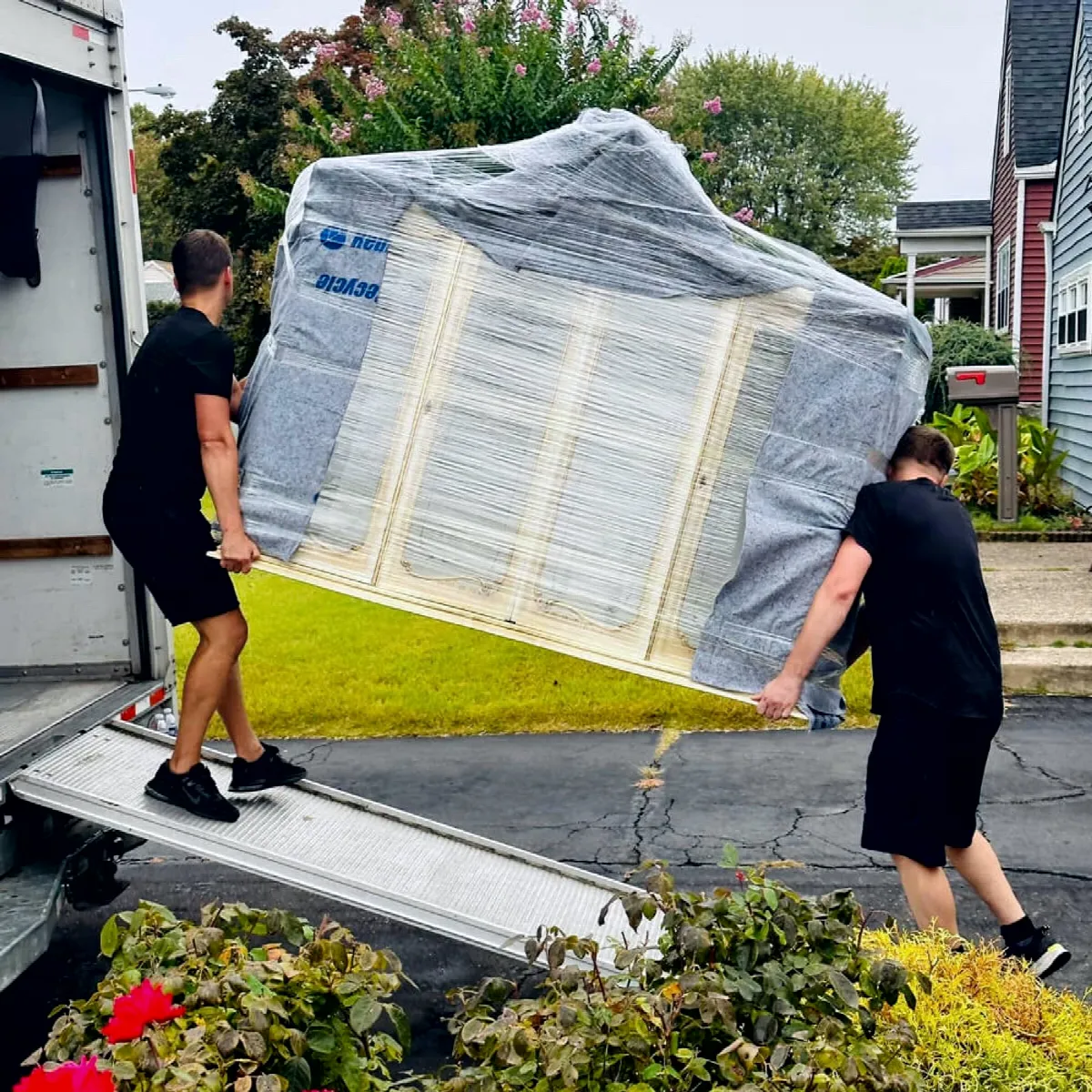 CarePhilly Movers carrying a wrapped sofa up the truck ramp