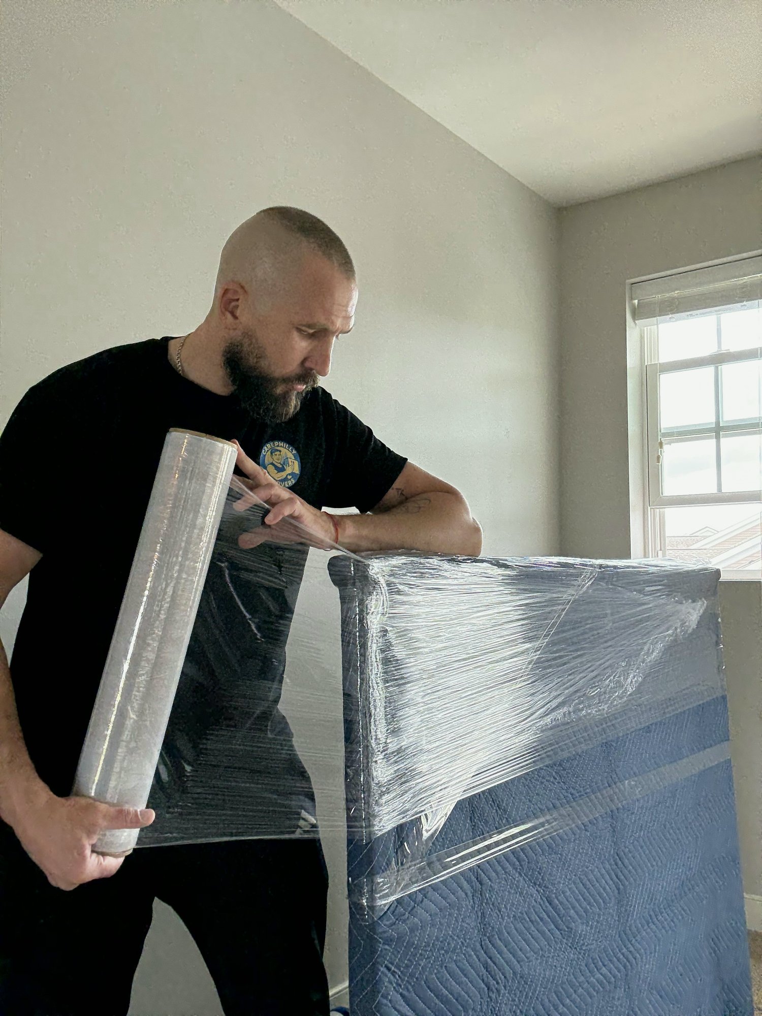 A mover wrapping a headboard in stretch film and moving blankets during packing services.
