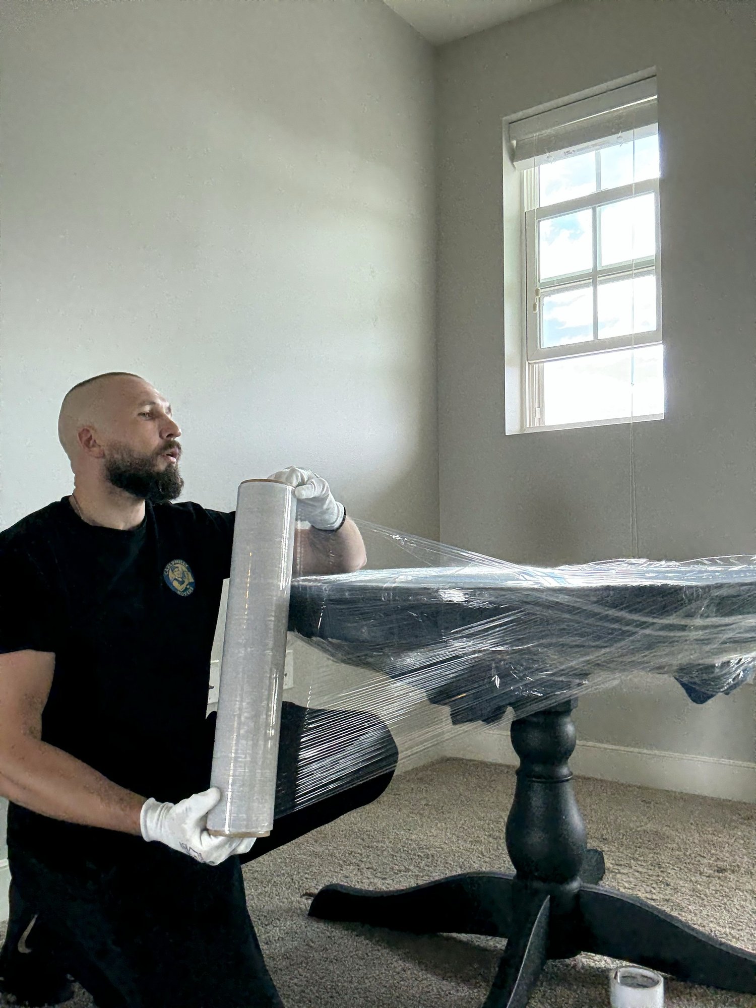 A mover wrapping a wooden table in stretch film during packing services.